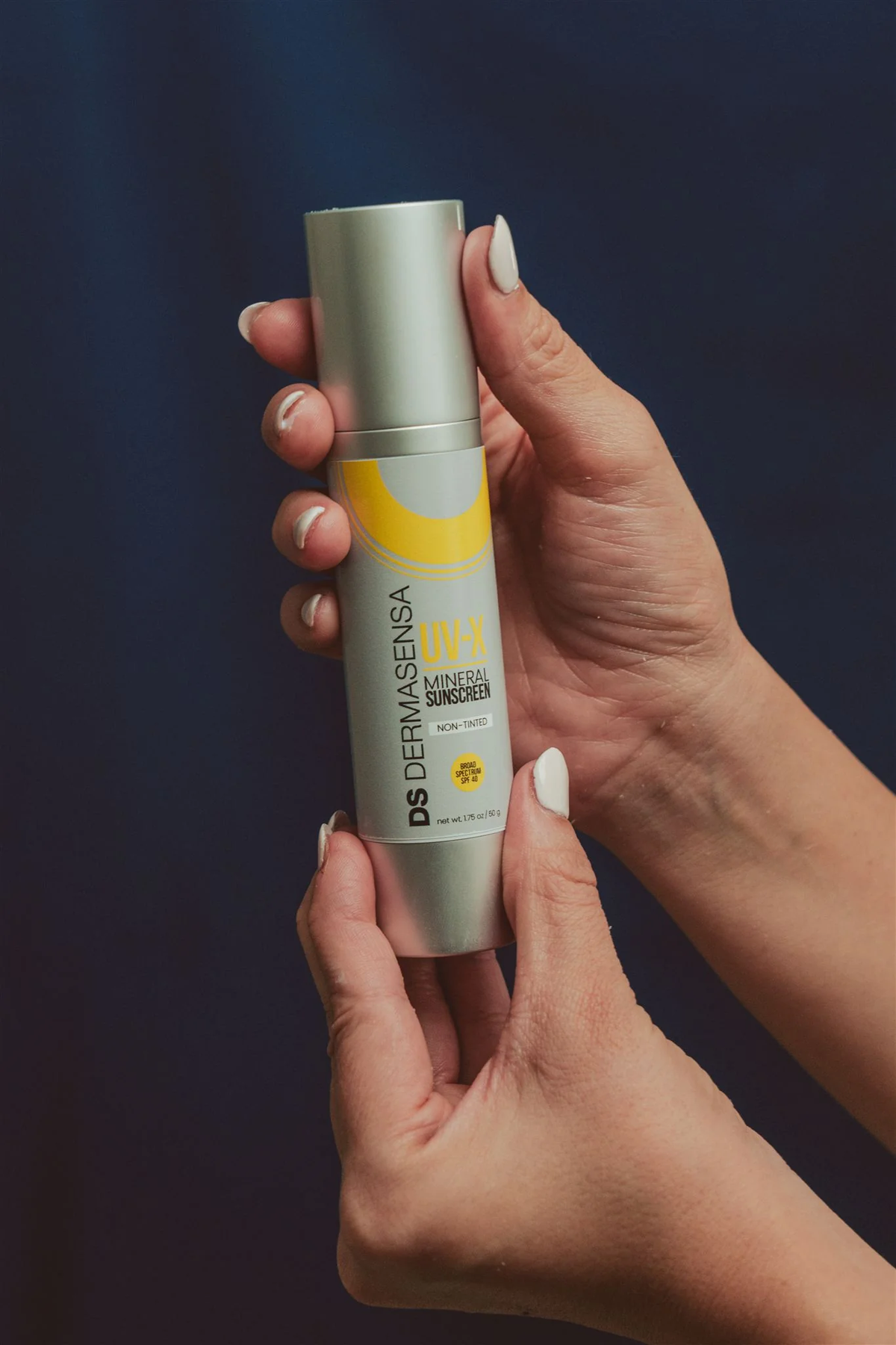 Dermasensa UV-X Mineral Sunscreen SPF 40 Non-Tinted, 1.75oz bottle held in two hands against a navy background
