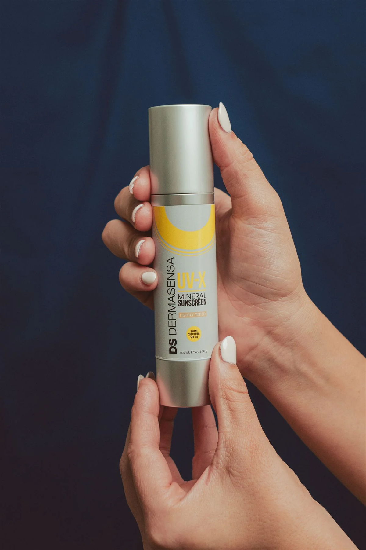 Dermasensa UV-X Mineral Sunscreen SPF 40 Lightly Tinted, 1.75oz bottle held in two hands against a navy background