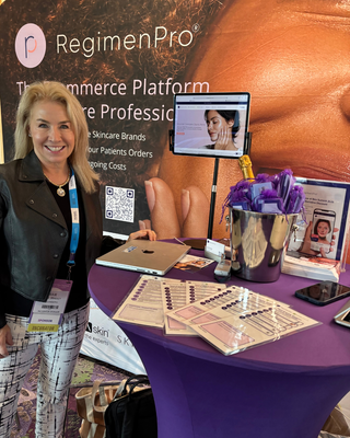 RegimenPro team member standing at a conference booth with a purple tablecloth and a tablet displaying the RegimenPro platform.