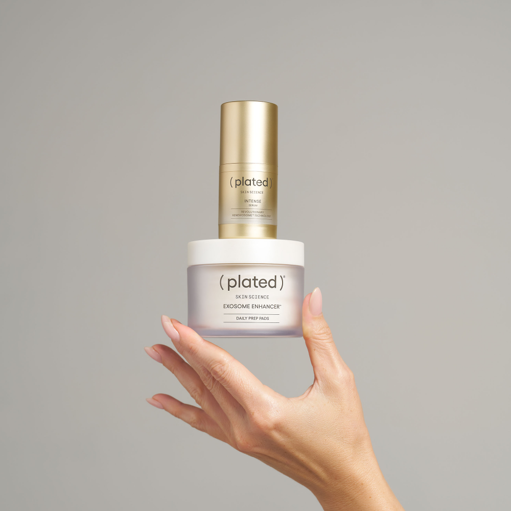 ( plated ) Skin Science, Exosome Enhancer Daily Prep Pads, 50 pads. Hand holding the jar with a gold ( plated ) INTENSE Serum bottle balanced on top.