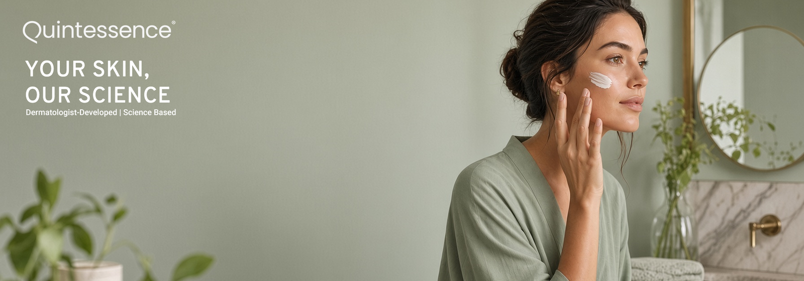 Quintessence banner reading “Your Skin, Our Science. Dermatologist-Developed | Science Based.” A woman in a sage green robe applies cream to her cheek in a green bathroom with a round mirror.