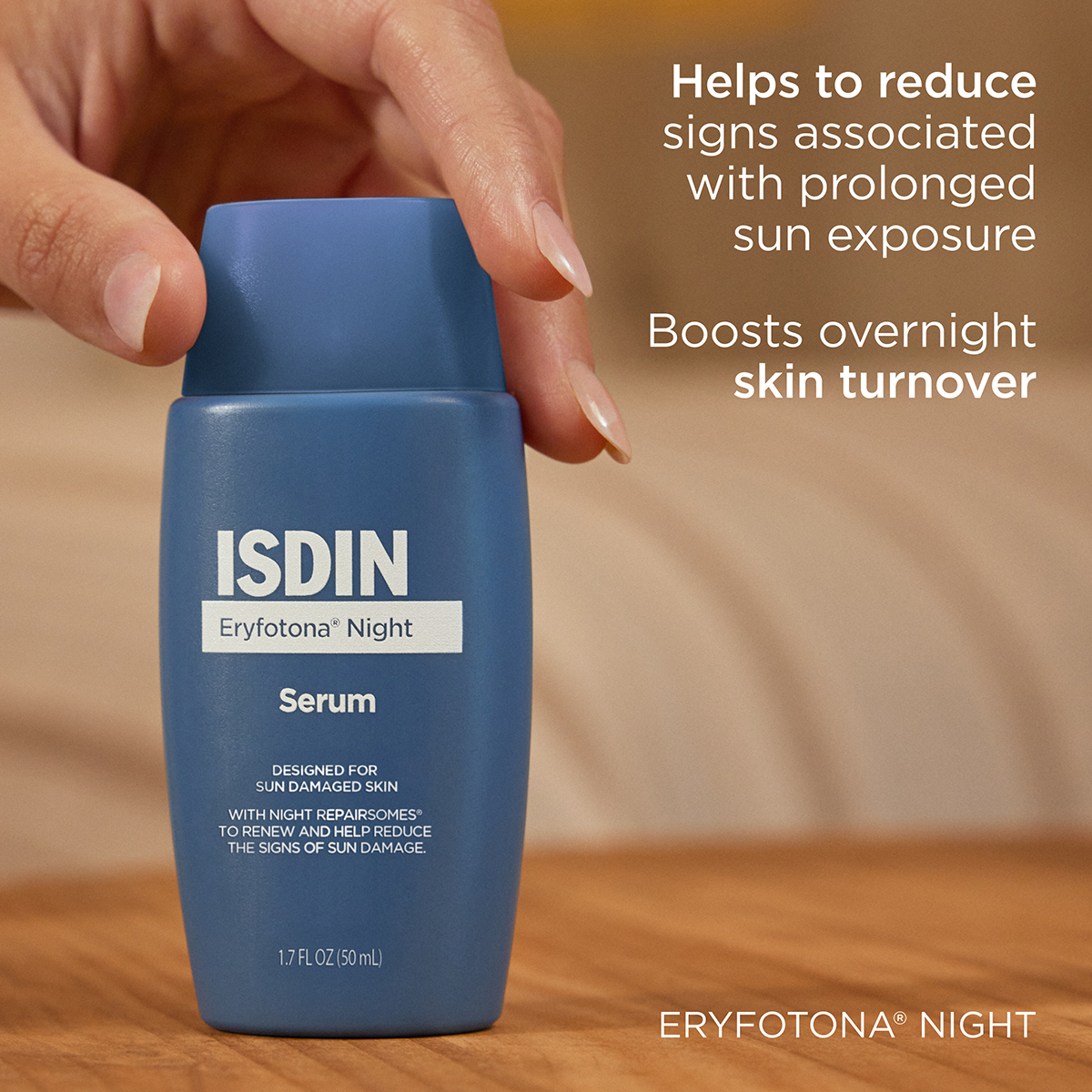 Blue ISDIN Eryfotona Night Serum bottle held by a hand on a wooden surface.